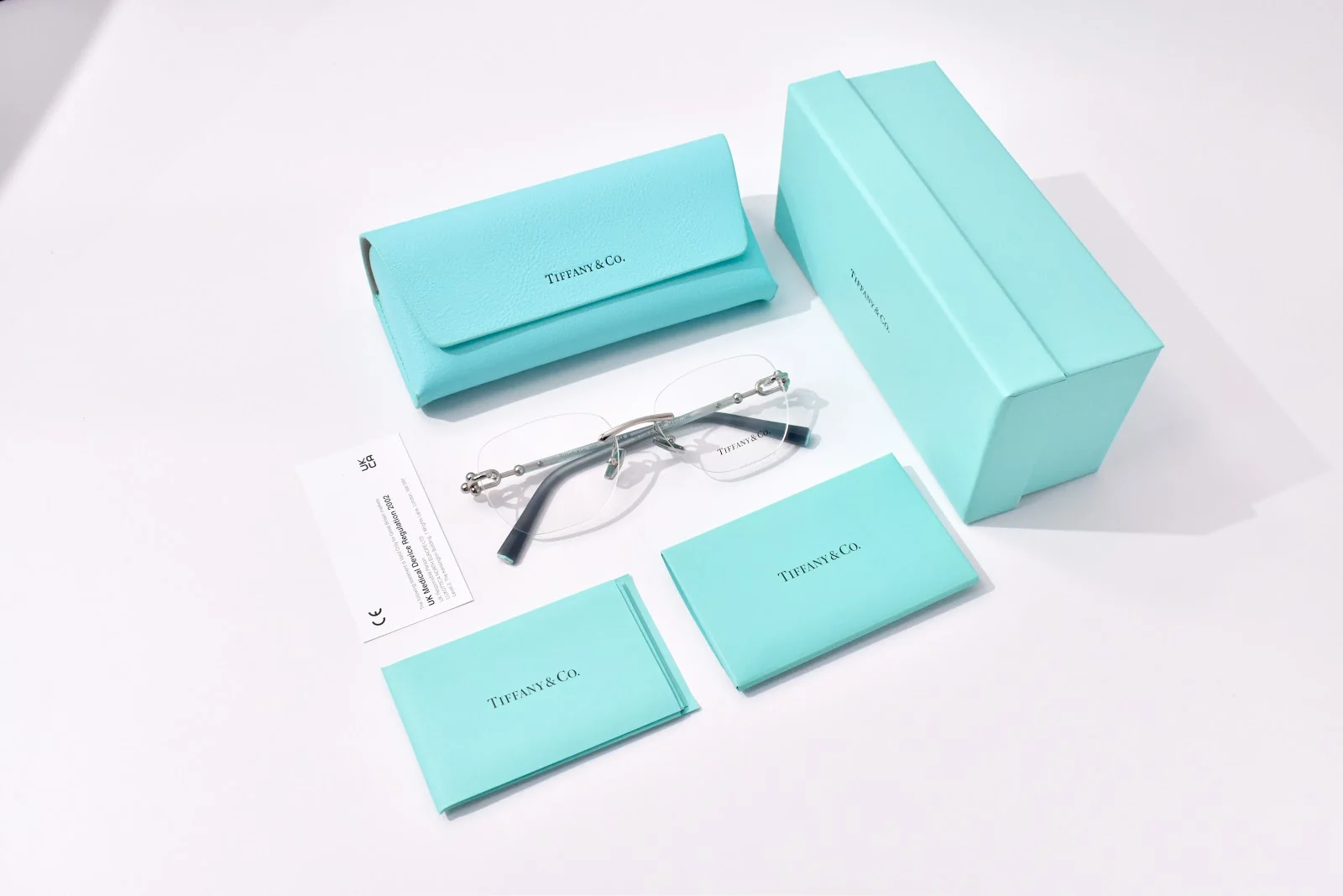 แว่นสายตาไร้ขอบ Tiffany & Co. TF1170D วางพร้อมกล่อง เคส และผ้าเช็ดแว่นสีฟ้า