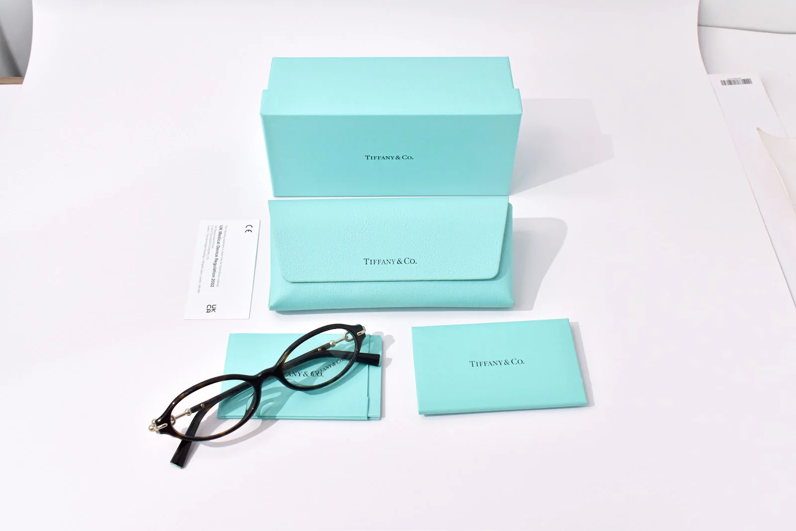 กรอบแว่นอะซิเตทสีเข้มทรงวงรี Tiffany & Co. TF2297F วางพร้อมกล่อง เคส และผ้าเช็ดแว่น